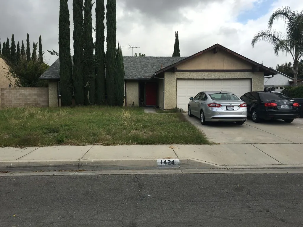 Single-story home at 1424 West Wabash Street in Rialto, California, with tall cypress trees and an attached garage.