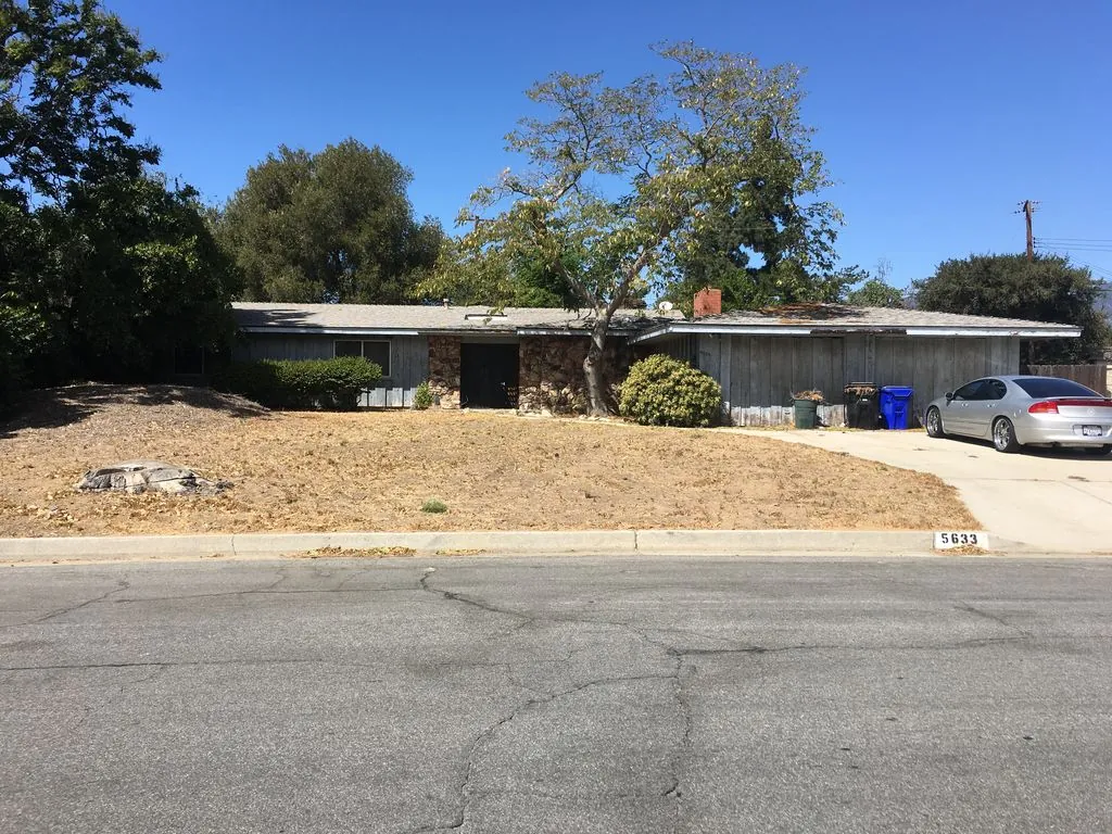 Single-story home at 5633 Magnolia in Rialto, California, with stone entry details, a mature tree and a dry front yard.